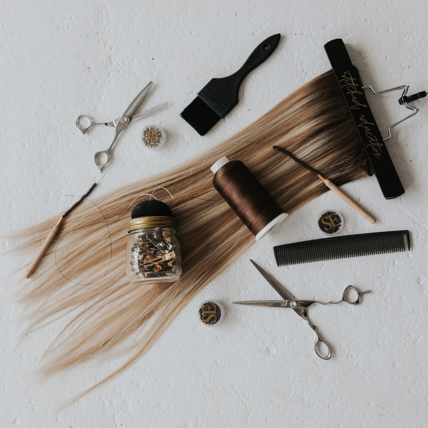 Hair extensions, thread, scissors, and salon tools flat lay on a white background representing returns and refunds process.