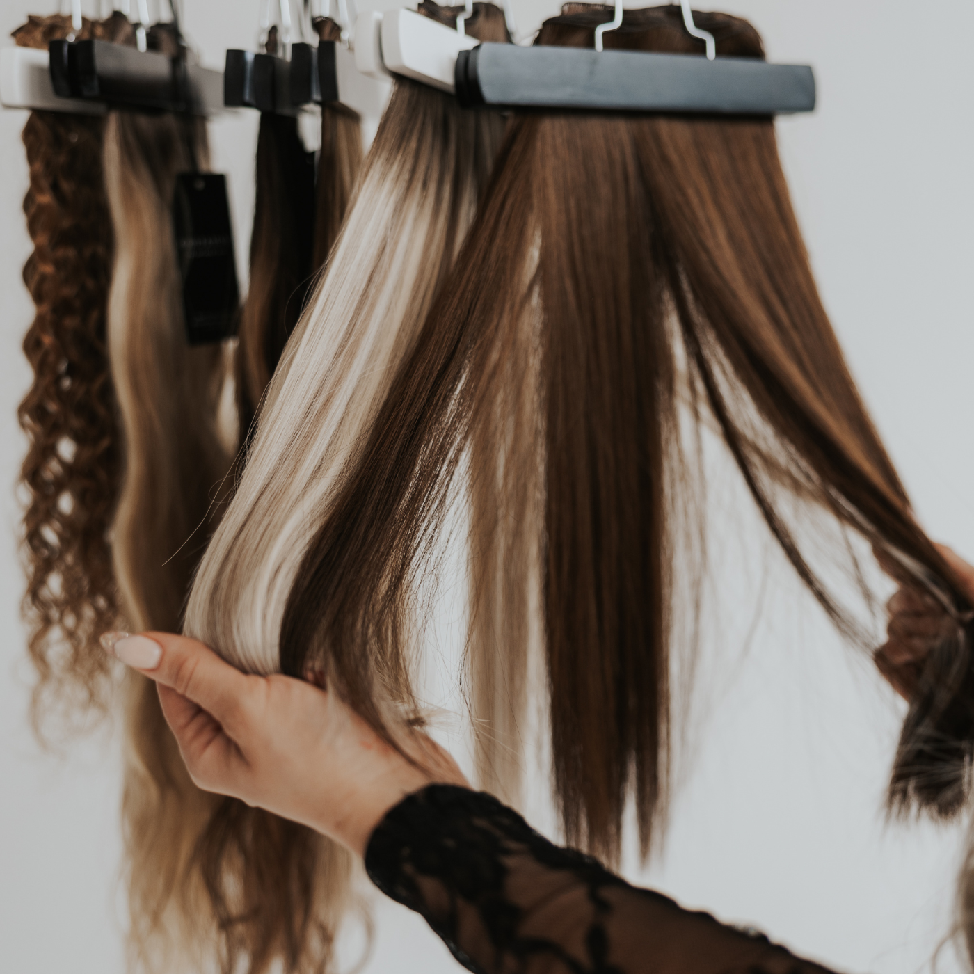 Hand holding swatches of Stitched™ hair extensions in various textures and colors.