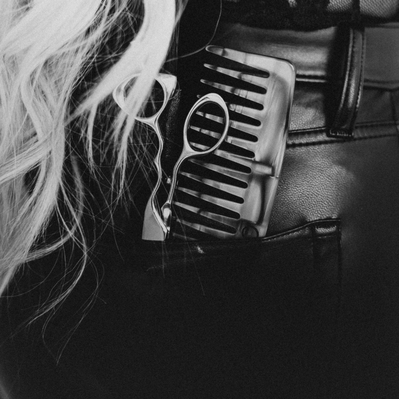 Stylist tools including scissors and a comb tucked into a pocket, with blonde hair in the frame.